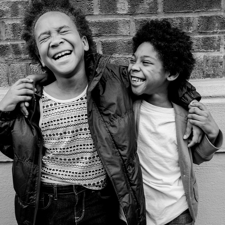 Two children smiling with their arms around eachother. 