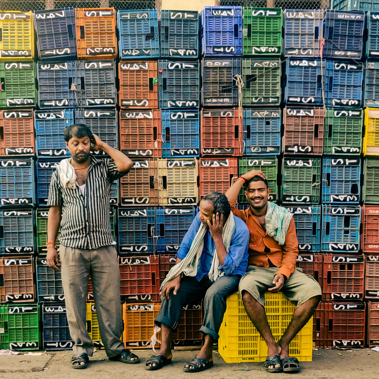 Three men standing and sitting surrounded by colorful crates. 