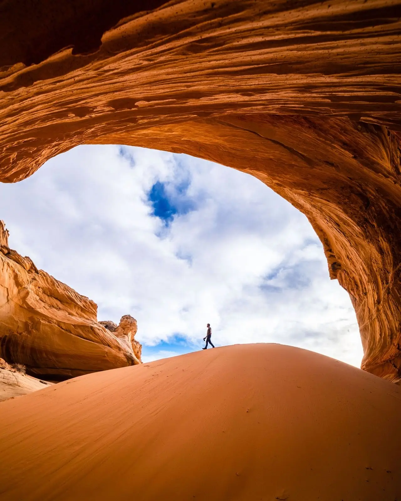 Photo of a person walking under red rock in the desert. 