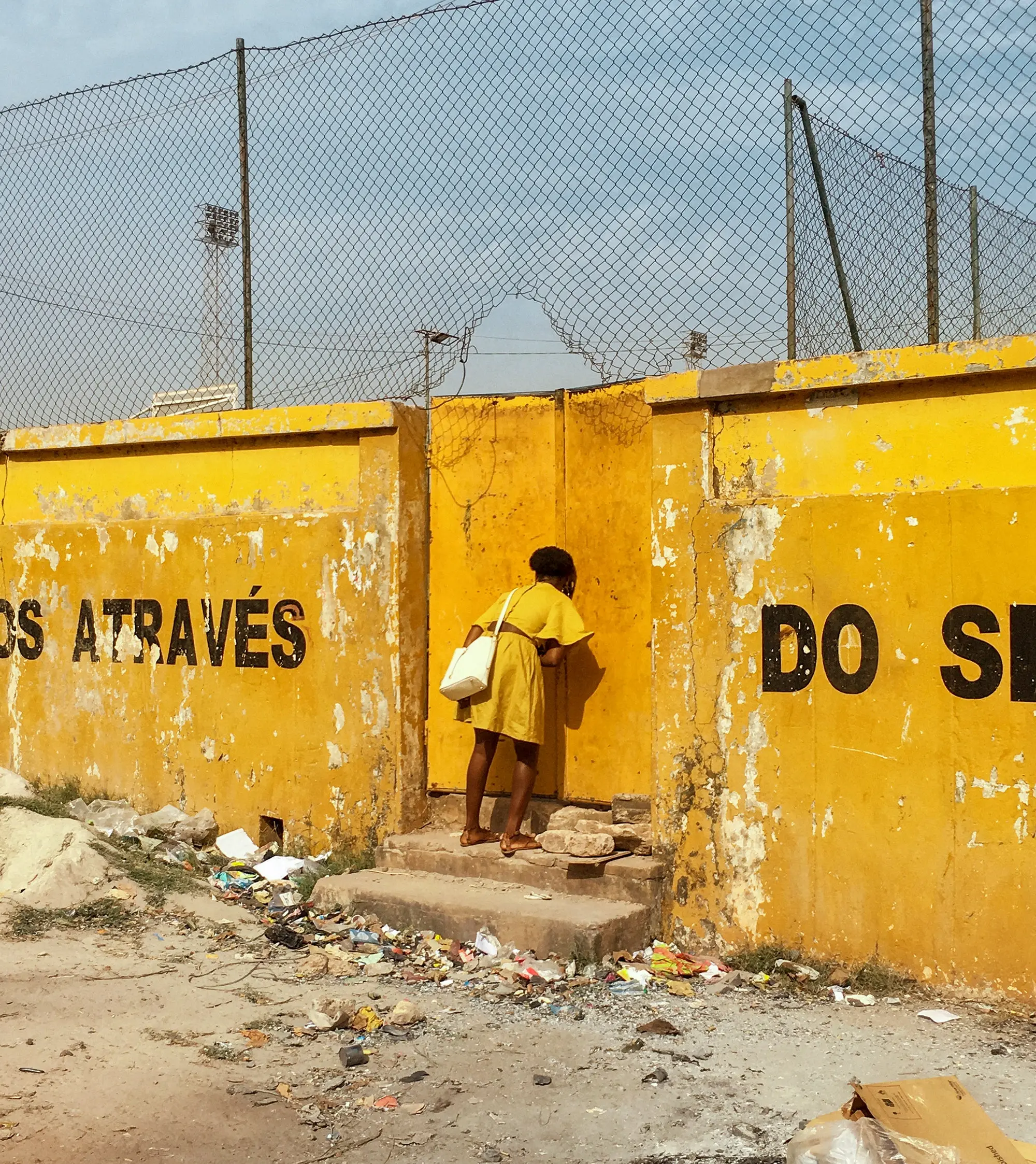 Image of woman wearing a yellow dress looking through a yellow wall. 