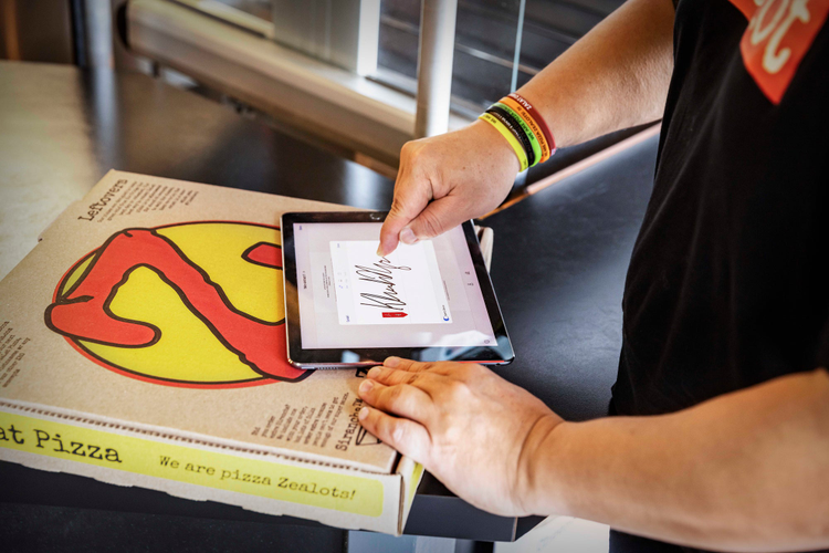 Ipad sitting on a pizza box being signed using Adobe Sign. 