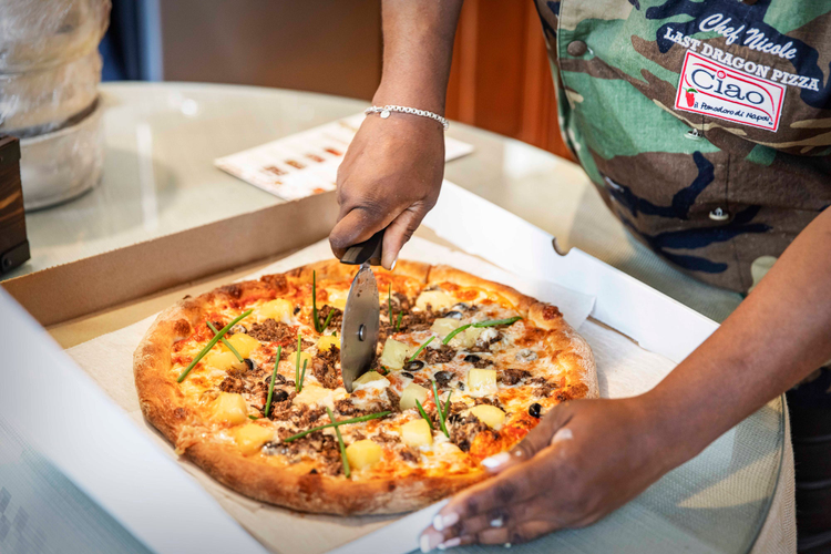 Pizza with pineapple being cut with a pizza slicer. 