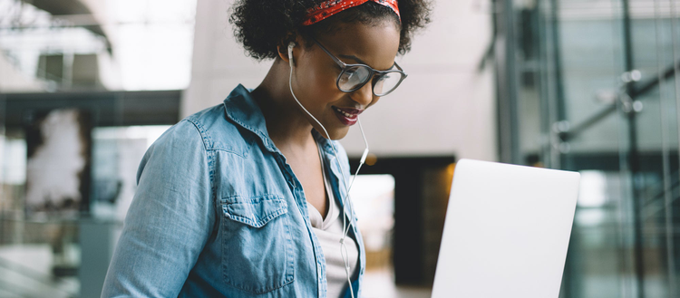 Woman with headphones in looking at a laptop screen. 