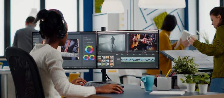 Woman working on two computer screens using video editing software.