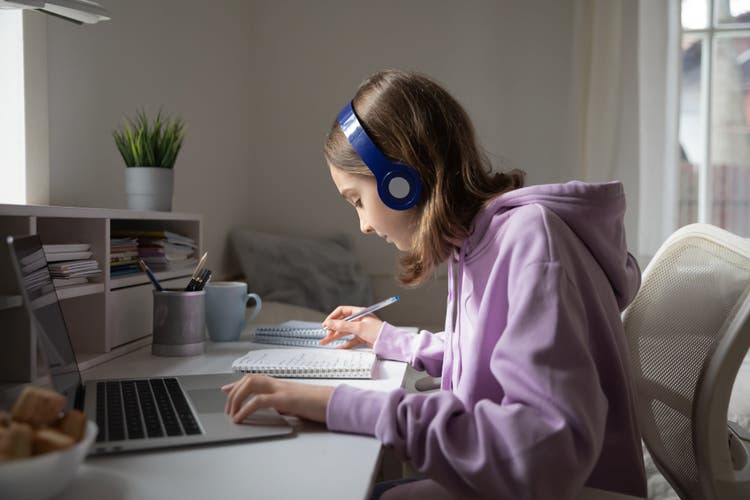 Image of college student sitting at desk with laptop and headphones.