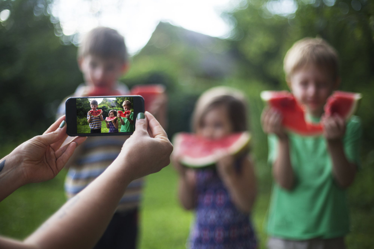 Picture being taken with a cell phone of kids eating watermelon. 