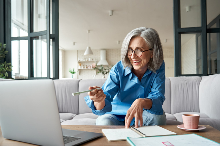 Happy mature older woman video calling on laptop working from home.