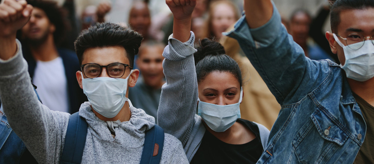 Group of poeople in masks with thier arm raised.