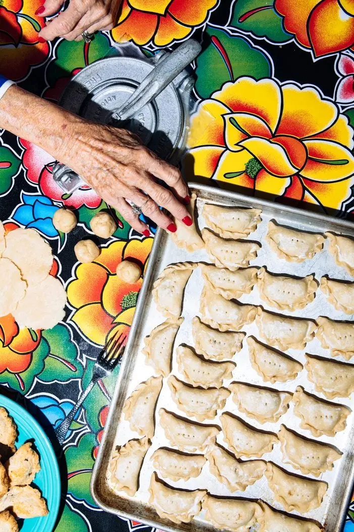 A hand reaching out to a pan full of empanadas. 