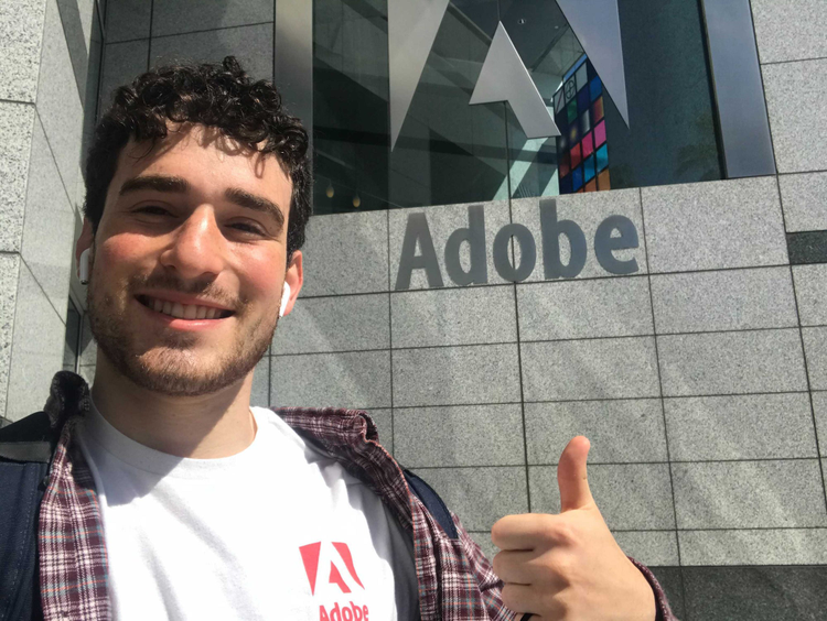 Bennett giving a thumbs up in front of the Adobe logo at headquarters.