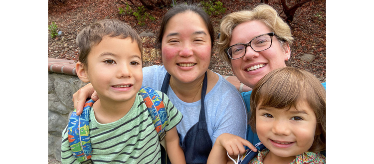 Laura Feeney (right) with her wife Dina and children Kai (age 6) and Rae (age 4). They are in their backyard smiling.