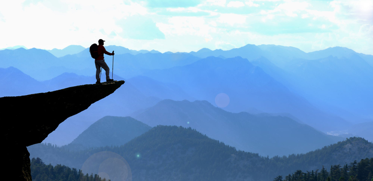 Man standing on the edge of a mountain looking over a valley. 
