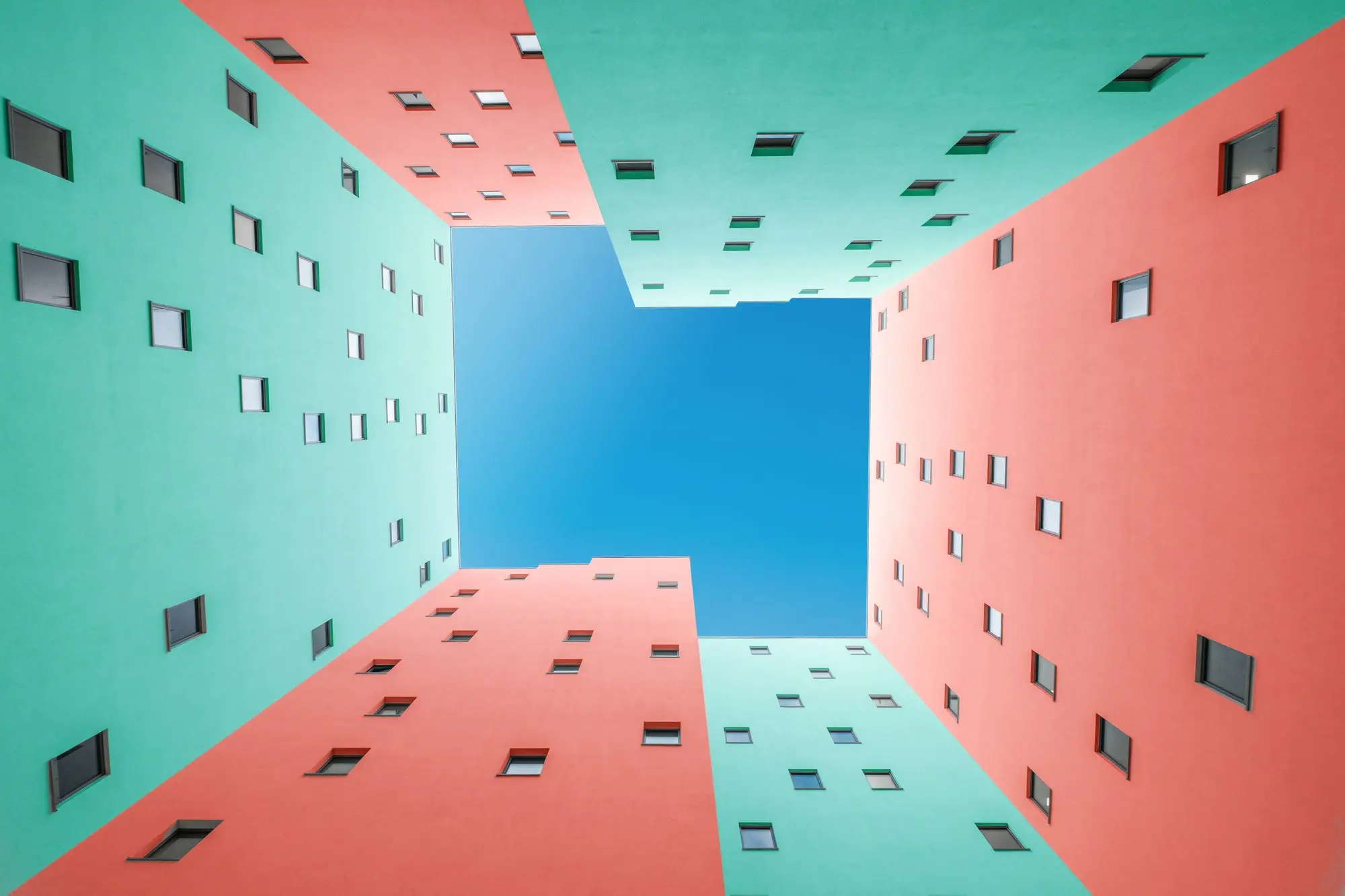 Pink and green buildings. Camera looking up toward the sky in between walls, making a blue shape. 