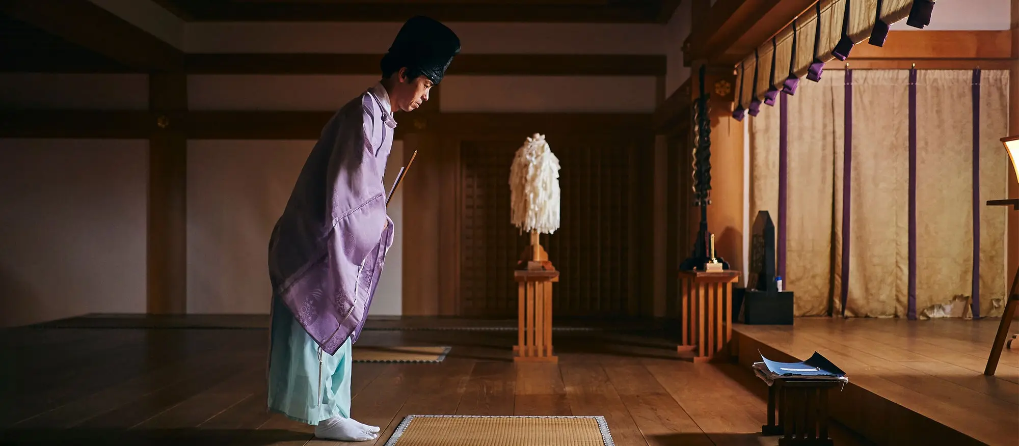 Man dressed traditionally, bowing over a mat. 
