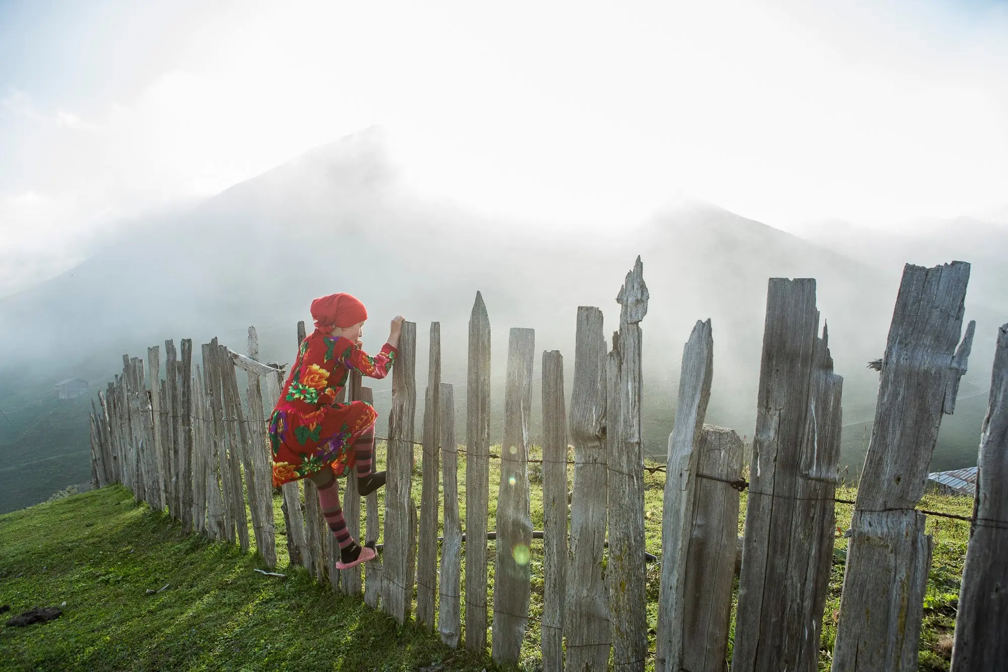 Person climbing a wooden fence surrounded by misty clouds. 