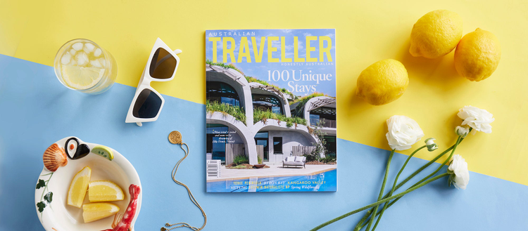 Image of Australian Traveller Media publication on a flat surface with sunglasses, flowers, lemons and ice water.