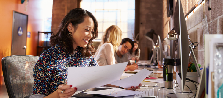 Woman looking over papers while sitting in front of a computer. 