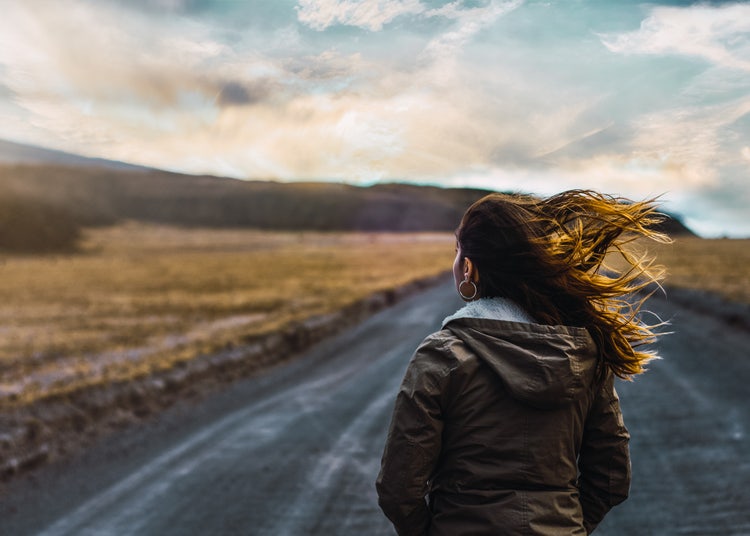 Photograph of a woman standing on a road in the wind.