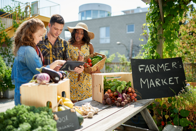 Friendly woman tending an organic vegetable stall at a farmer's market and selling fresh vegetables from the rooftop garden.