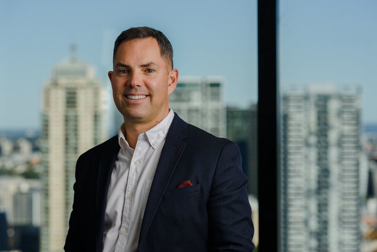 Colin Campbell smiling. He is dressed in a suit, with the Sydney skyline behind him.