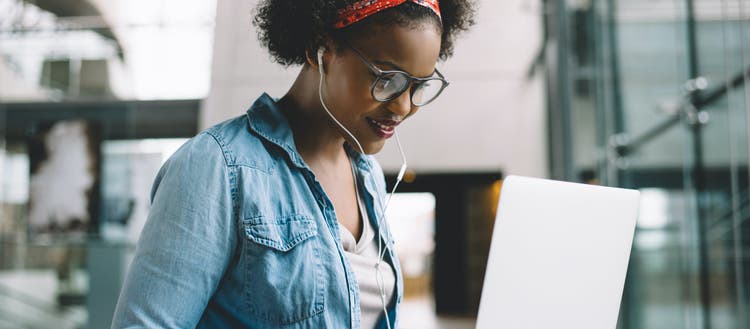 Woman with headphones in looking at a laptop screen.