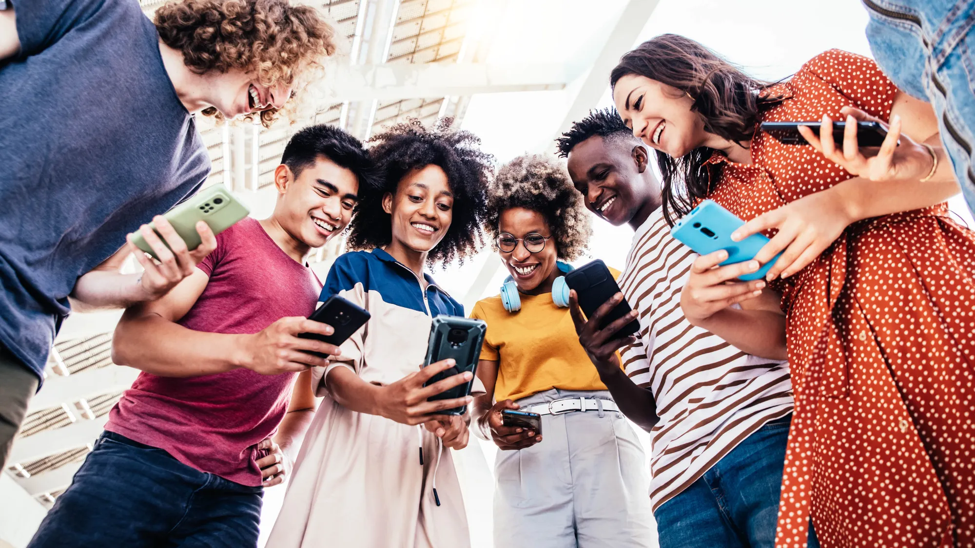 Diverse teenage students using digital smart mobile phones on college campus - Group of friends watching cellphones sharing content on social media platform.