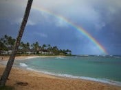 A photo of a rainbow over the ocean on a beach.