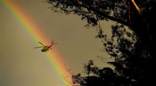 A photo of a rainbow in the sky. In front of it there's a helicopter.
