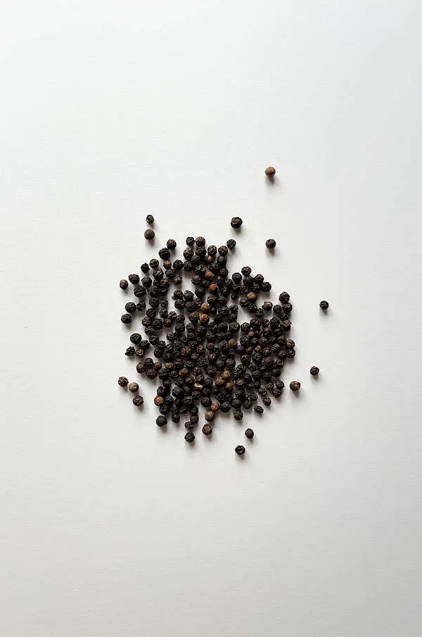 An overhead shot of peppercorns on a white table using a standard 35mm lens.
