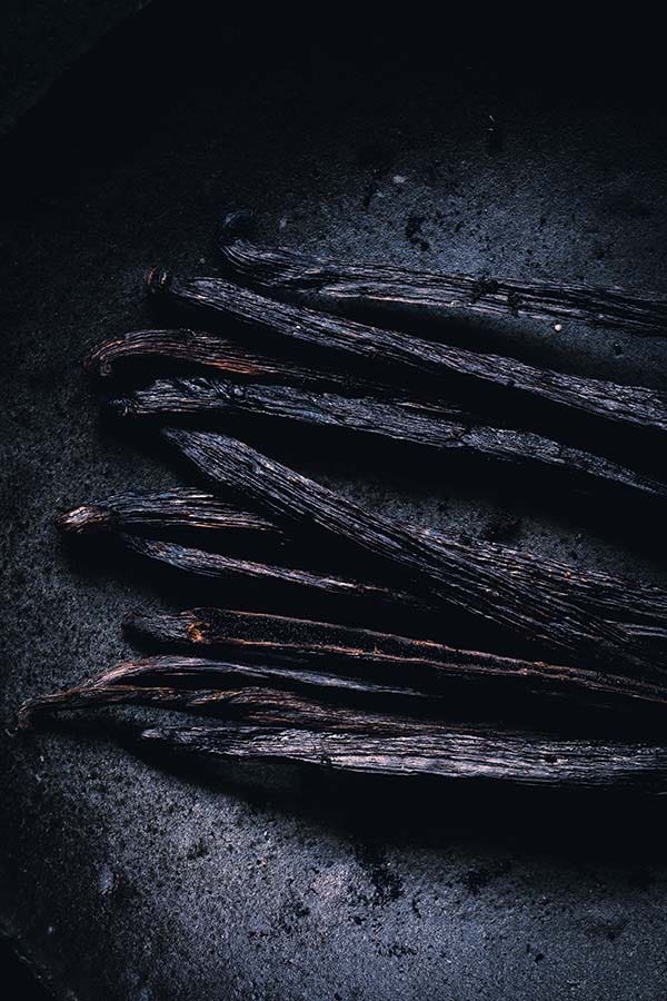 Macro photography of vanilla bean pods placed on a ceramic plate.