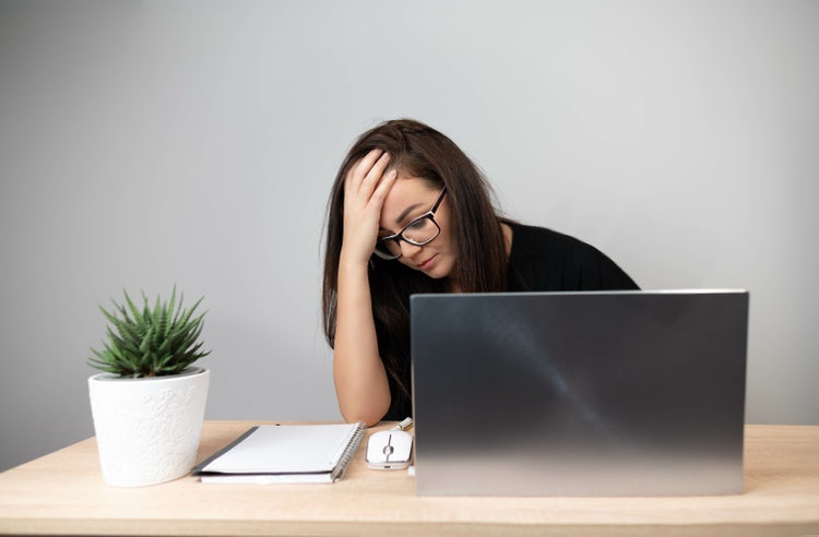 Stressed tired exhausted businesswoman sitting at office desk with laptop and notebook.