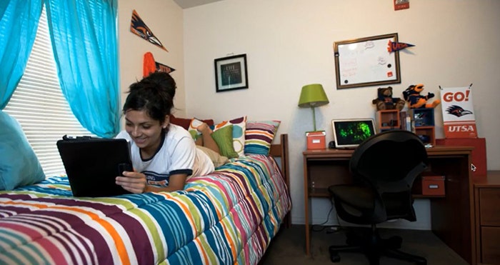 College student laying on bed using an electronic device.