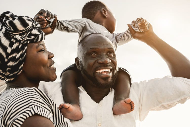 Family smiling with baby sitting on shoulders.