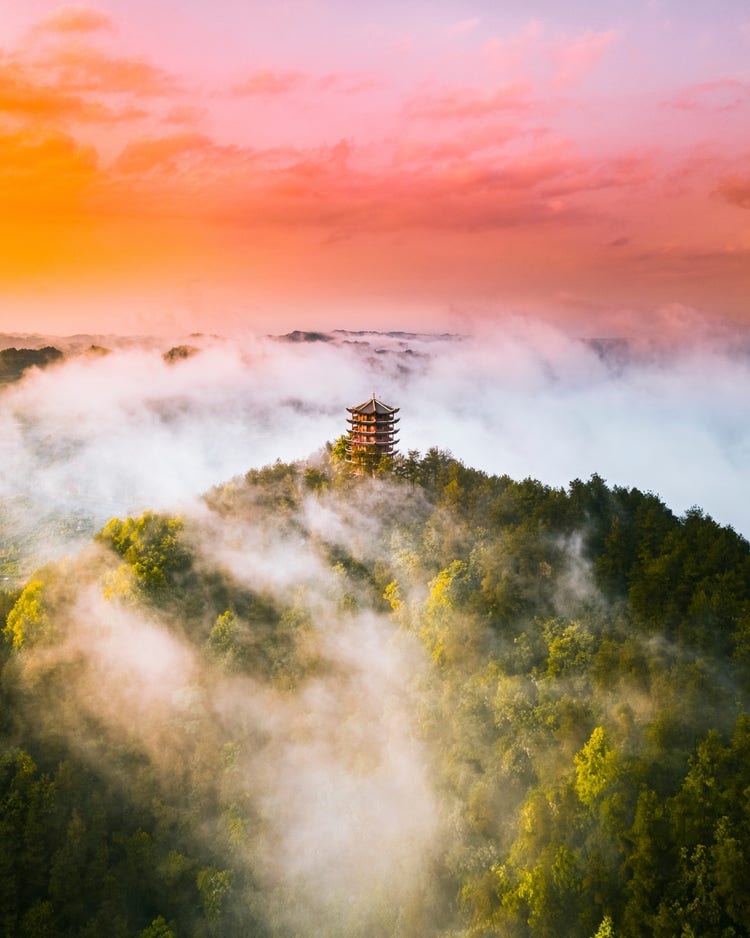 Cloudy view of a buiding set on top of a green mountain. 