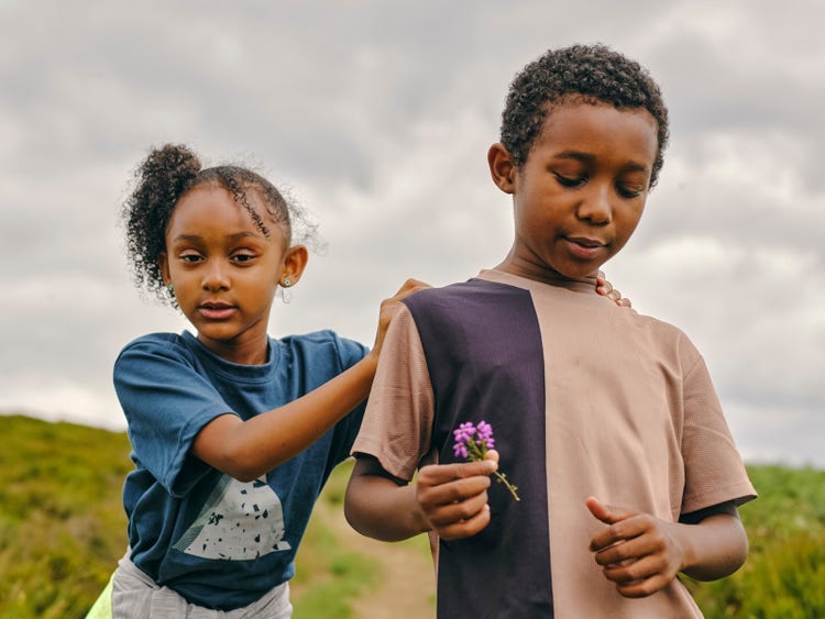 Two children outdoors holding a small flower. 