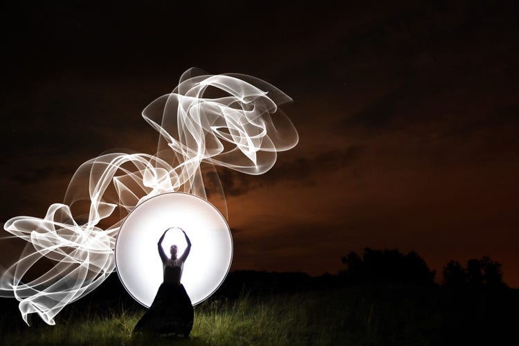 Dark image of woman lit up by swirls of light.