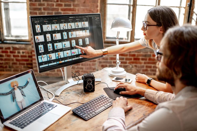 Young couple of photographers working with woman's portraits at the working place with two computers in the studio.