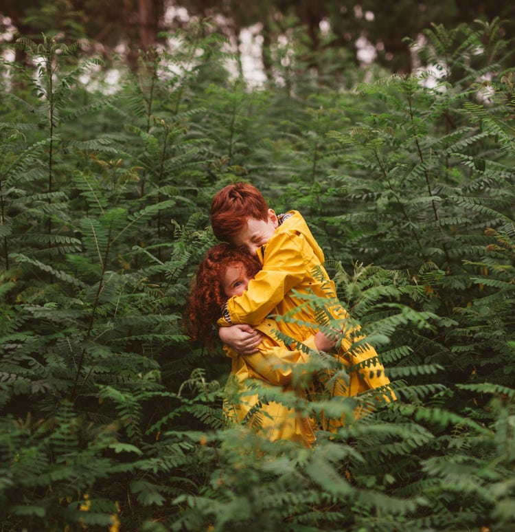 Image of two children wearing yellow jackets in the middle of green bushes. 
