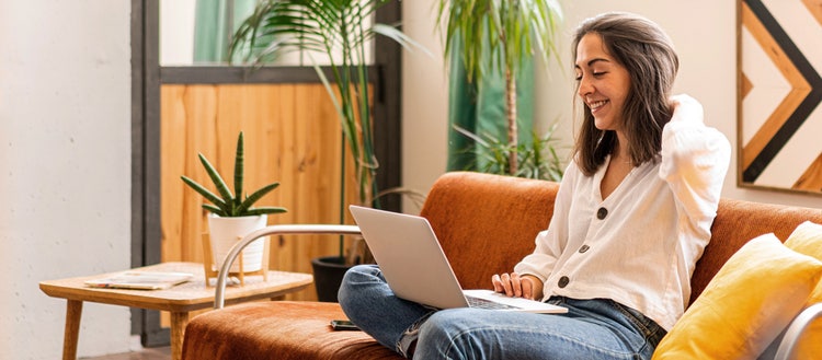 Woman on a couch looking at her laptop.