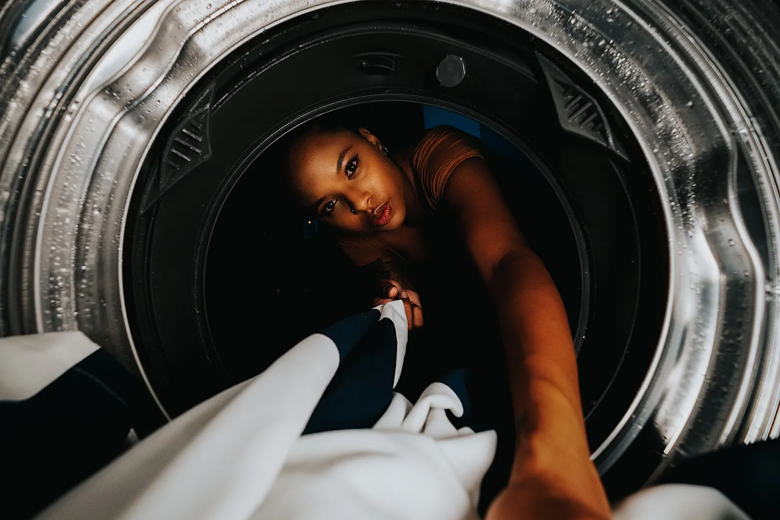 Self portrait of Chinelle Rojas taken with a Fujifilm XT-4. The camera is inside a dryer machine and facing her as she reaches in.