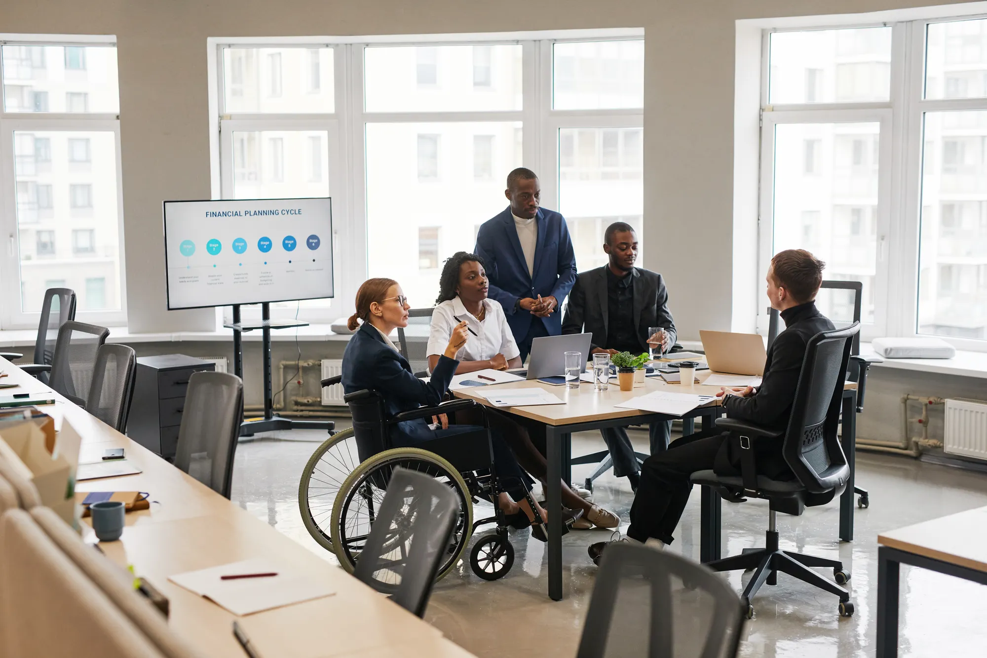 Diverse group of business people at meeting table in office with woman using wheelchair in leadership.