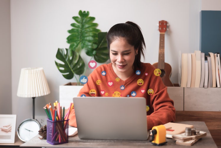 Women working on laptop with emoji coming off the screen.