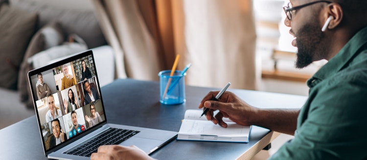 Man on a laptop, taking notes during a team meeting. 