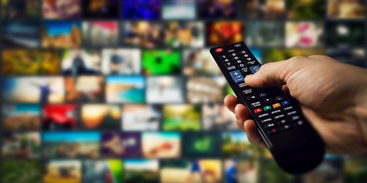 Tv channels in background and remote control in hand.