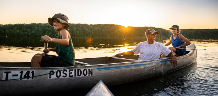 Air-force service member takes his sons canoeing at sunset out on the lake.