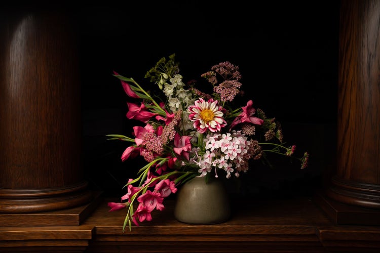 Vase with a variety of flowers on a wooden ledge between two pillars. Light falloff produces a natural vignette around the vase.