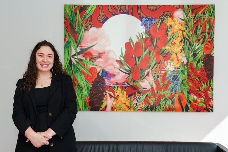 Wiradjuri and Ngiyampaa person, Charlotte Allingham standing next to her artwork.