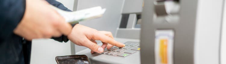 Persons hand hold a wallet with cash and withdraw some money in atm.