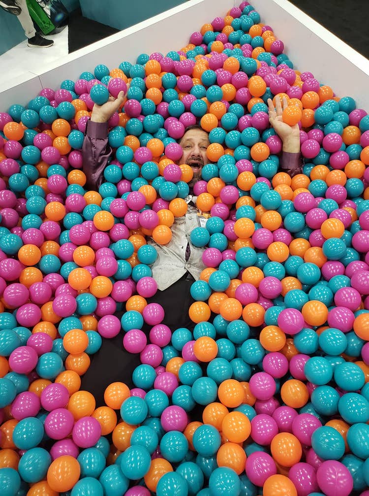 Dax smiles laying on his back with arms raised in a pool of plastic balls that almost cover him completely that was created as an interactive display at Adobe MAX 2022.