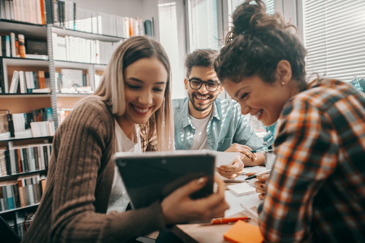 Students in a library looking at a tablet